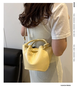 Detail of a yellow patent leather bucket bag featuring a knotted handle and shoulder strap