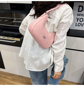 Detailed side view of pink crescent shoulder bag with silver bow accent on model