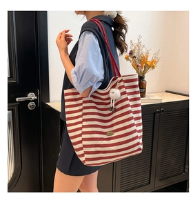 Macro detail of red striped canvas tote bag with shoulder strap and plush charm