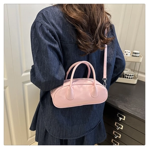Detailed view of pink leather baguette bowling bag worn as a crossbody with denim dress