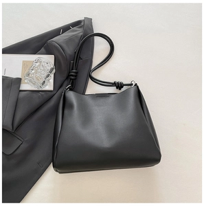 Minimalist black tote bag with knot shoulder strap detail on grey blazer background