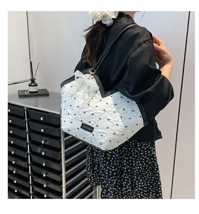 Detail of white tote bag with black bow print and large pearl lace charm accessory