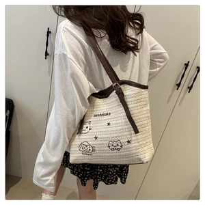 Close-up of woven straw tote bag with brown leather straps and cute cat embroidery