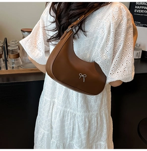 Brown crescent shoulder bag with silver bow detail shown on white lace dress model