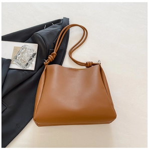 Detail of caramel leather tote bag with decorative knot strap on a stylish background