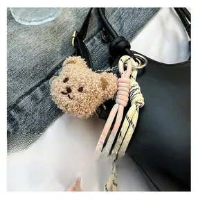 Dettaglio di un ciondolo a forma di orsetto di peluche beige con corde intrecciate colorate