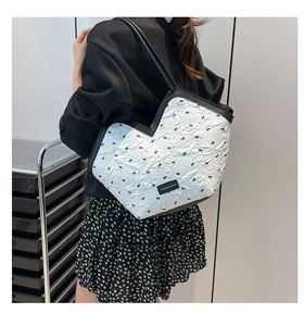Detail of heart-shaped quilted tote bag featuring black bow patterns and fashion label
