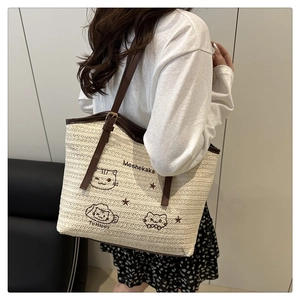 Close-up of woven straw tote bag with brown leather handles and cute embroidered cats