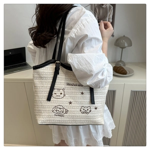 Detail of straw tote bag featuring cute embroidered cats and black leather shoulder straps