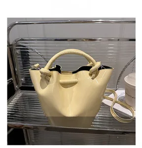 Detail of pale yellow patent leather bucket bag with knot handle and metal logo imprint