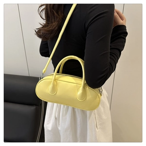 Detail view of a bright yellow Boston bag featuring smooth texture and metallic top zipper