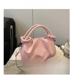 Detail of pink pleated cloud bag featuring leather handles and adjustable shoulder strap