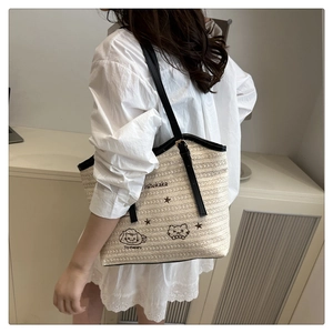 Detail of hand-woven straw tote with black cat embroidery on a female model shoulder