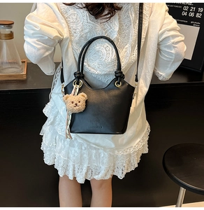 Detail of black PU leather bucket bag with plush bear charm on white lace dress