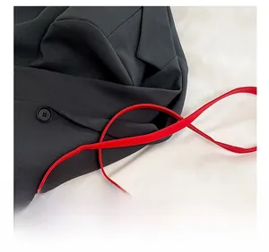 Détail du sac carré en cuir mat rouge avec bandoulière posé sur un blazer noir