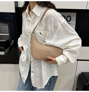 Beige crescent underarm bag with silver bow detail worn with a casual white shirt