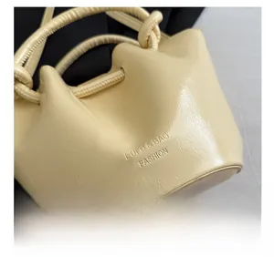 Close-up of beige pleated bucket bag featuring embossed text and woven spiral handle
