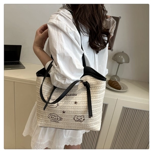 Detail of hand-woven straw tote bag with black leather straps and cat embroidery