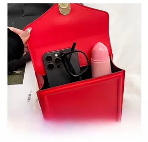 Détail macro montrant l'intérieur spacieux du sac bandoulière en cuir rouge et objets
