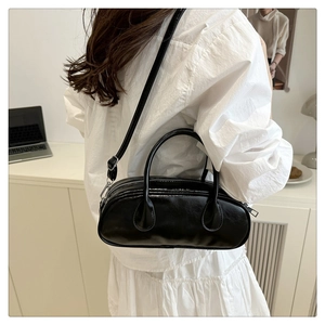 Detail of a black shiny Boston bag with top handles and adjustable shoulder strap