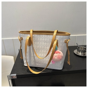 Close-up of white quilted tote bag with yellow straps and pink plush pendant