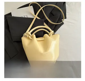 Détail du sac seau en cuir jaune clair avec poignée et texte embossé sur costume gris