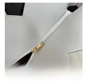 Detail of smooth gold zipper on white textured leather tote bag with fine stitching