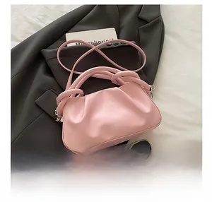 Detailed view of pink pleated dumpling bag with knotted handle on a black suit blazer