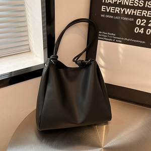 Minimalist black leather tote bag with knotted rope shoulder strap on a metal table