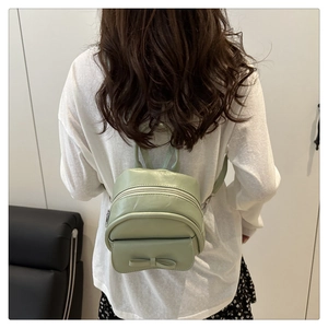 Mint green cloud backpack with bow detail worn by a model in a casual setting