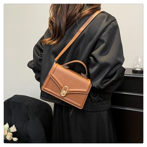 Gros plan du sac bandoulière marron avec boucle dorée porté à l'épaule par un mannequin