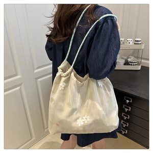 Detail of floral embroidery on cream-colored organza drawstring shoulder tote bag