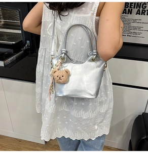 Close-up of metallic silver bucket bag with round handles and cute plush bear charm