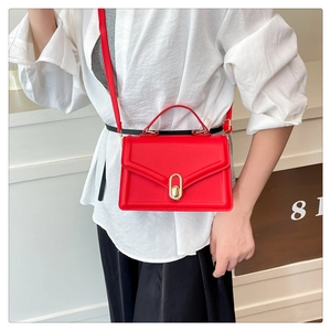 Détail du sac bandoulière rouge en cuir avec fermoir doré porté par le modèle