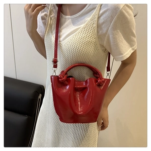 Détail du sac seau en cuir verni rouge avec poignée nouée et logo gaufré sur le sac