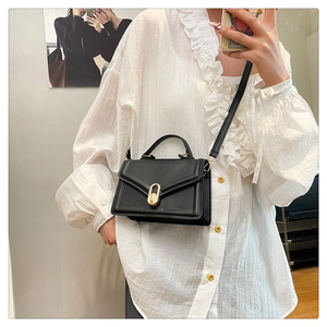 Detail of black leather crossbody bag featuring an oval gold metal turn-lock closure