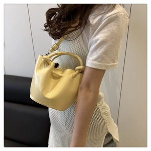 Detail of light yellow bucket bag with glossy finish and unique knotted handle design