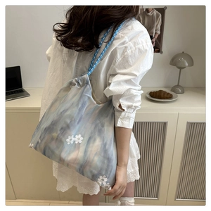 Detail of blue ink-wash tote bag featuring delicate floral embroidery and woven straps
