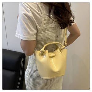 Detail of light yellow bucket bag with knotted handle and glossy patent leather finish