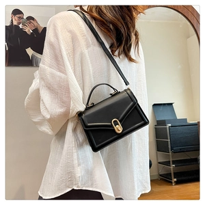 Vue latérale d'un sac bandoulière carré en cuir noir porté par un mannequin dans une pièce