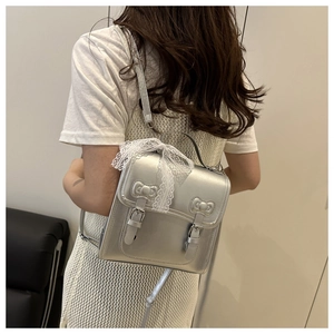 Detail of silver metallic backpack featuring bow accents and a white lace ribbon detail