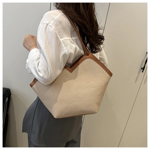 Close-up of woven straw tote bag featuring brown leather trim and V-shaped top design