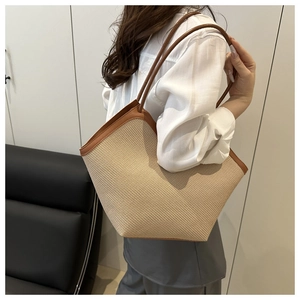 Detail of a beige woven straw tote bag with brown leather straps worn on shoulder