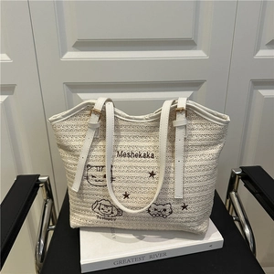 Straw tote bag with cat embroidery and adjustable leather straps on a vintage chair