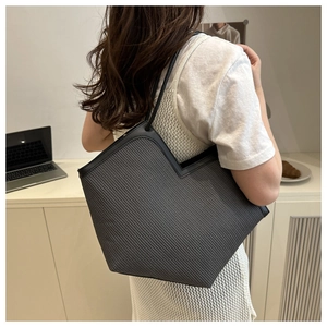 Detail of grey woven tote bag with black trim and V-shaped top worn by model
