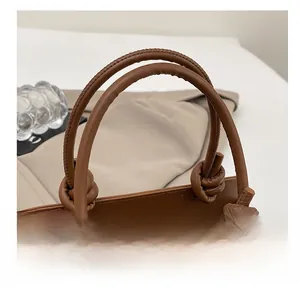 Detail of knotted handle and crocodile embossed texture on brown crossbody saddle bag