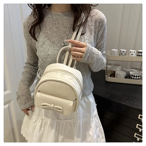 Close-up of a mini off-white backpack featuring a decorative bow and smooth matte PU leather