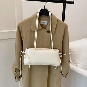 Sac à bandoulière blanc rectangulaire avec nœuds sur un fond de trench-coat kaki