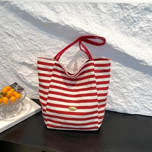 Striped canvas tote bag with red handles and handmade metal plate on a white stone background