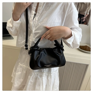 Detail view of black pleated leather handbag with logo lettering and thin shoulder strap